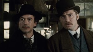 Robert Downey Jr. and Jude Law look intently at something with their heads tilted in Guy Ritchie's Sherlock Holmes.