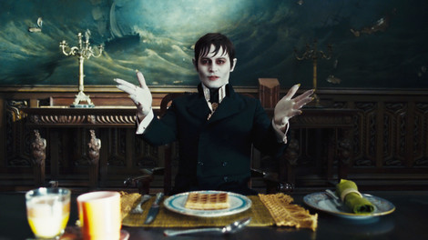 Johnny Depp in Dark Shadows sitting at a table with his hands out.