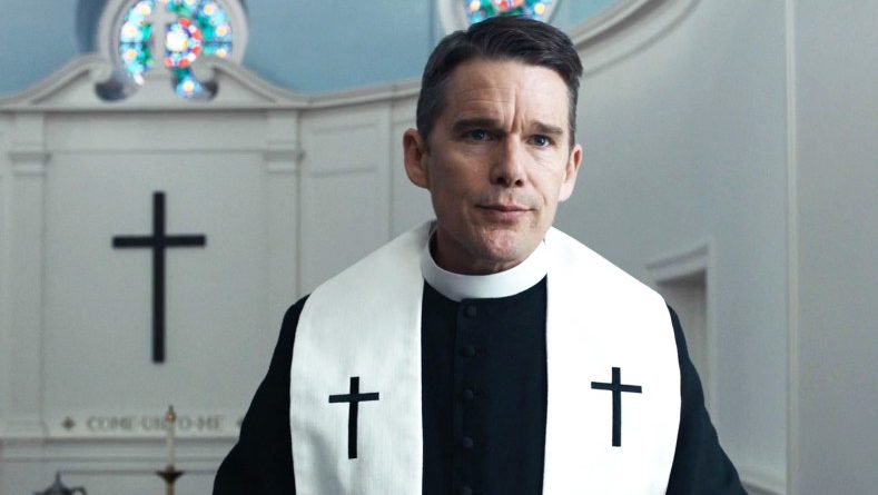 Ethan Hawke dressed as a minister in a church with his lips pursed in Paul Schrader's movie First Reformed.