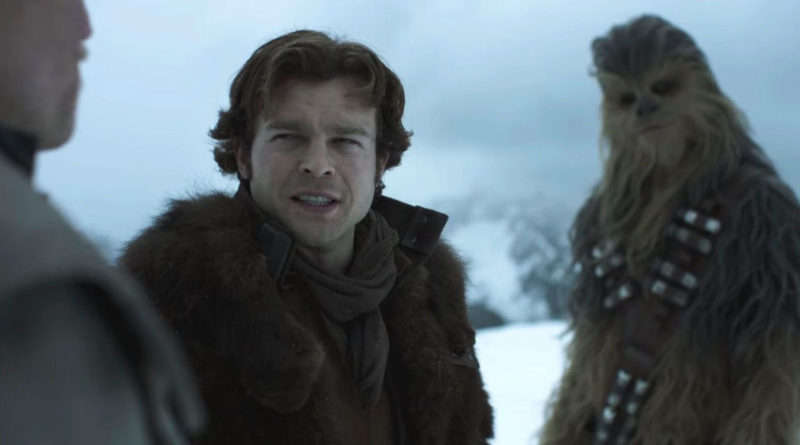 Alden Ehrenreich in Solo: A Star Wars Story talking to Woody Harrelson in the foreground while Chewbacca stands in the background with his head tilted.
