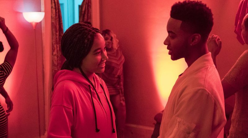 Amandla Stenberg and Algee Smith in the reddish glow of a party looking at each other and smiling in the film The Hate U Give