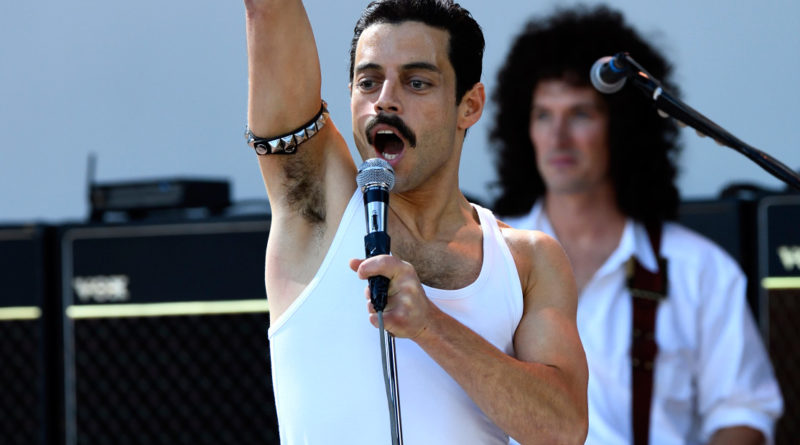 Rami Malek as Freddie Mercury in the film Bohemian Rhapsody singing at Live Aid with one arm in the air