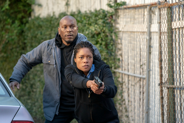 Tyrese stands behind Naomi Harris who is pointing a gun protecting him in the movie Black and Blue