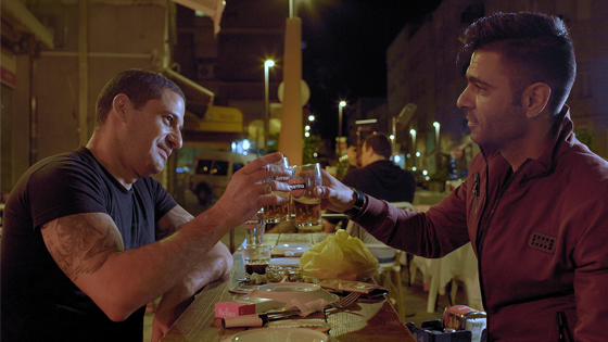 A Jewish and an Arab chef toast as they eat food and enjoy each other's company in the documentary Breaking Bread