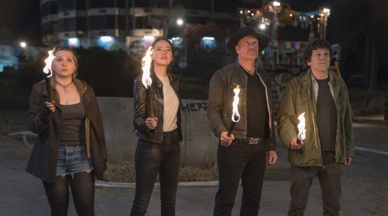 Abigail Breslin, Emma Stone, Woody Harrelson, and Jesse Eisenberg stand with lit torches looking up in the movie Zombieland: Double Tap