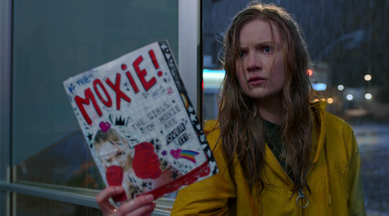 Hadley Robinson stands in the rain holding her zine as Vivian in Moxie