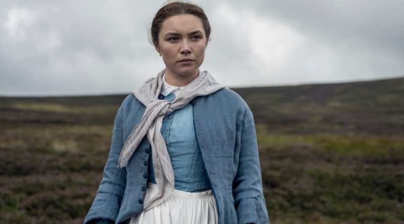 Florence Pugh looks stern standing in a field with an overcast sky in the movie The Wonder.